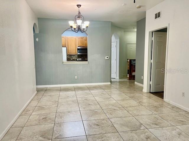 empty room featuring arched walkways, a chandelier, baseboards, and light tile patterned flooring
