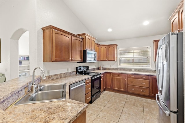 kitchen featuring stainless steel appliances, a sink, vaulted ceiling, light tile patterned flooring, and light countertops