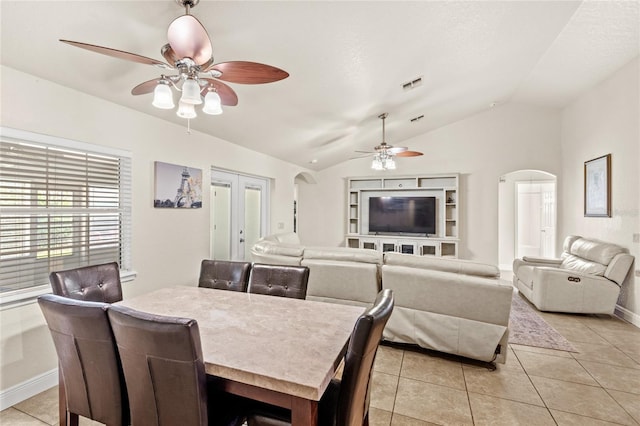 dining space featuring ceiling fan, arched walkways, vaulted ceiling, light tile patterned flooring, and baseboards