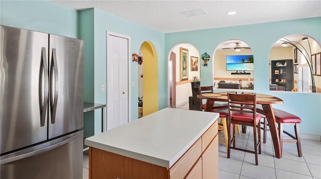 11257 Dacre Ln, Orlando, FL 32824 - kitchen featuring freestanding refrigerator, arched walkways, a center island, a textured ceiling, and light tile patterned floors