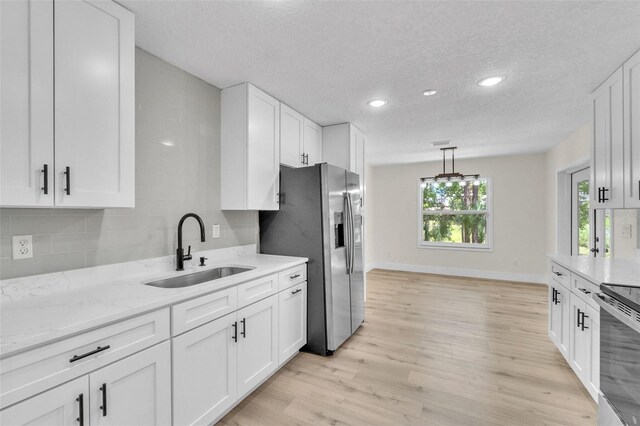 kitchen featuring a sink, appliances with stainless steel finishes, light wood-type flooring, tasteful backsplash, and white cabinetry