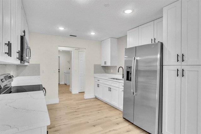 kitchen featuring stainless steel appliances, a sink, light wood-style flooring, white cabinetry, and recessed lighting