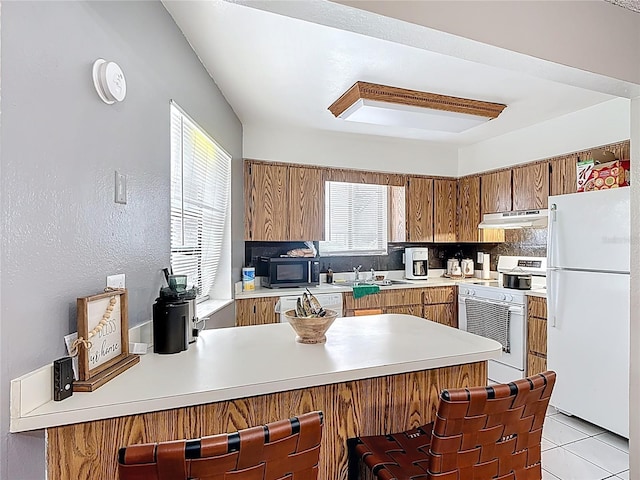 1803 Foxhall Cir Unit 1803, Kissimmee, FL 34741 - kitchen with white appliances, under cabinet range hood, a peninsula, brown cabinets, and light countertops