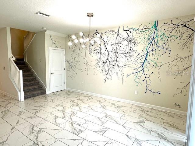 1513 Maidstone Ct, Davenport, FL 33896 - empty room featuring marble look tile flooring, stairs, a chandelier, a textured ceiling, and baseboards