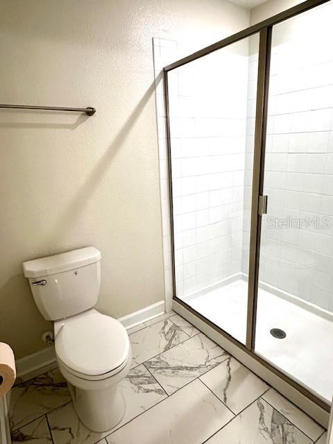 1513 Maidstone Ct, Davenport, FL 33896 - bathroom featuring marble look tiles, baseboards, toilet, and a stall shower