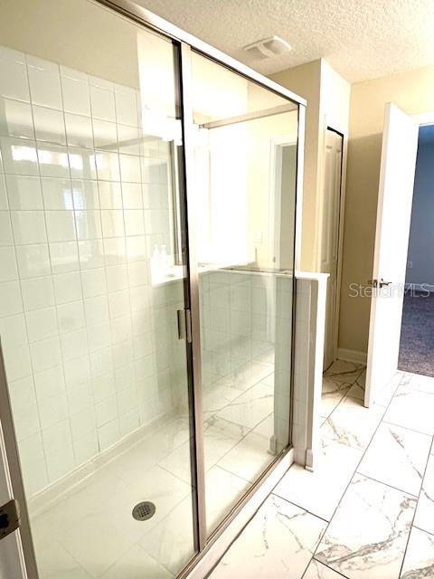 1513 Maidstone Ct, Davenport, FL 33896 - bathroom featuring marble finish flooring, a textured ceiling, and a shower stall