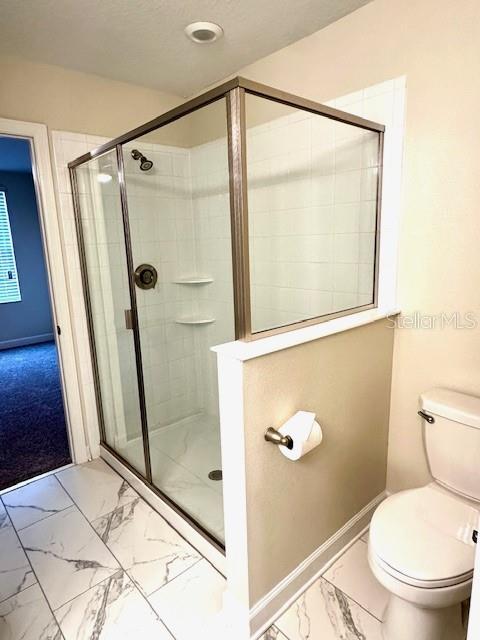 1513 Maidstone Ct, Davenport, FL 33896 - bathroom with marble look tile flooring, toilet, a shower stall, and baseboards