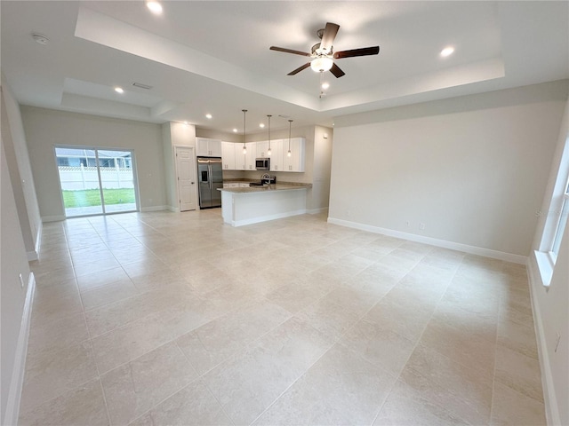unfurnished living room with a tray ceiling, ceiling fan, recessed lighting, baseboards, and light tile patterned floors