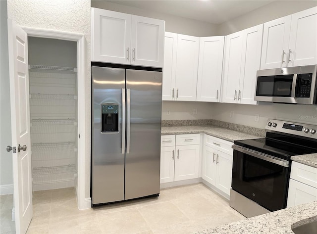 kitchen featuring stainless steel appliances, white cabinetry, light stone countertops, and light tile patterned floors