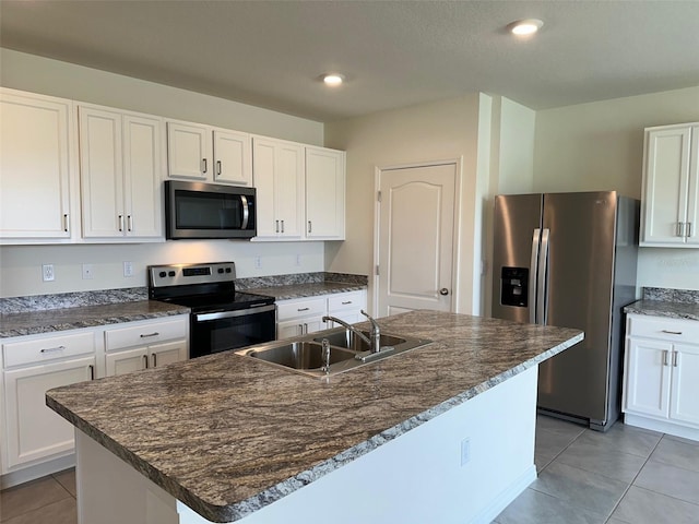 kitchen with stainless steel appliances, a sink, light tile patterned floors, white cabinets, and an island with sink
