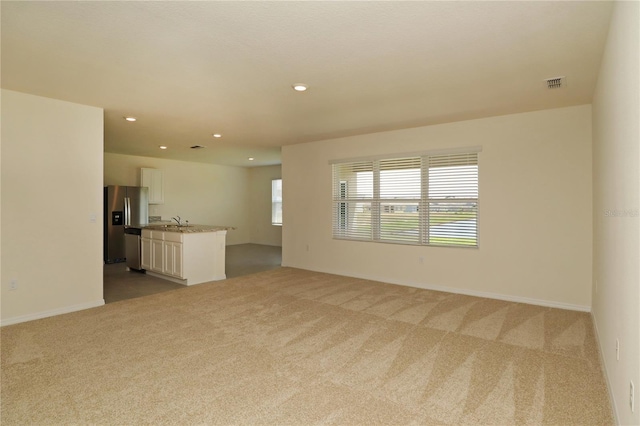 unfurnished living room with carpet flooring, a sink, recessed lighting, and baseboards