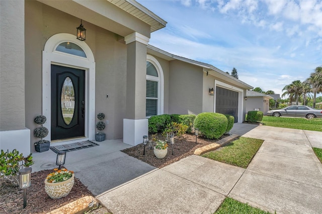 view of exterior entry featuring stucco siding, concrete driveway, and a garage