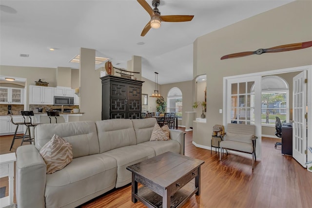 living room featuring a ceiling fan, wood finished floors, arched walkways, vaulted ceiling, and baseboards