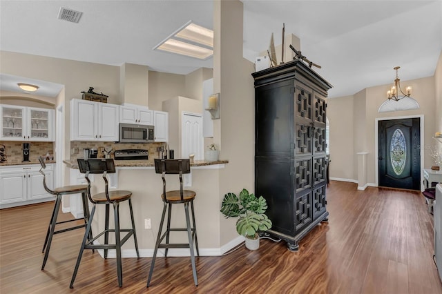 kitchen featuring stainless steel microwave, backsplash, a kitchen bar, and white cabinets