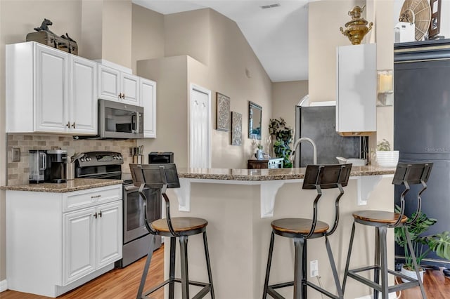 kitchen with appliances with stainless steel finishes, light wood-style floors, a breakfast bar, tasteful backsplash, and high vaulted ceiling