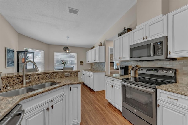 kitchen with appliances with stainless steel finishes, a sink, light wood finished floors, tasteful backsplash, and a textured ceiling