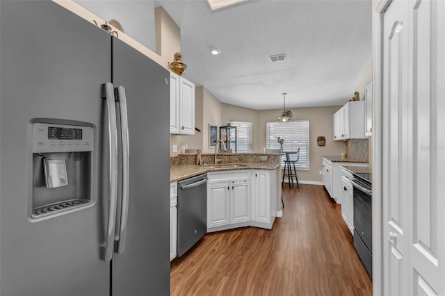 kitchen featuring stainless steel appliances, a sink, a peninsula, dark wood-type flooring, and white cabinetry