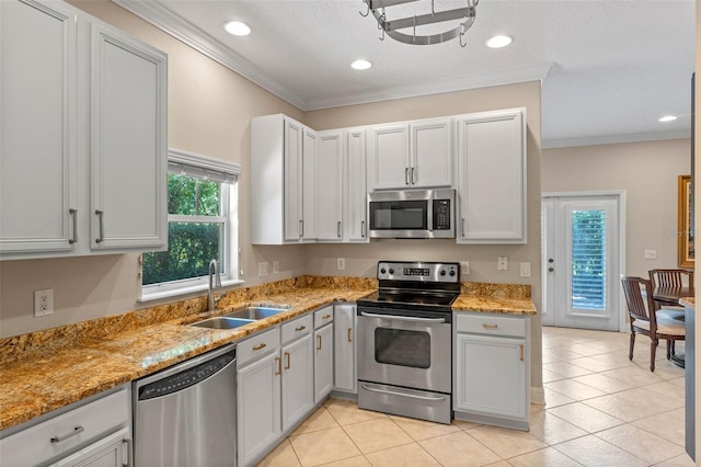 kitchen with appliances with stainless steel finishes, a sink, light stone counters, crown molding, and light tile patterned floors