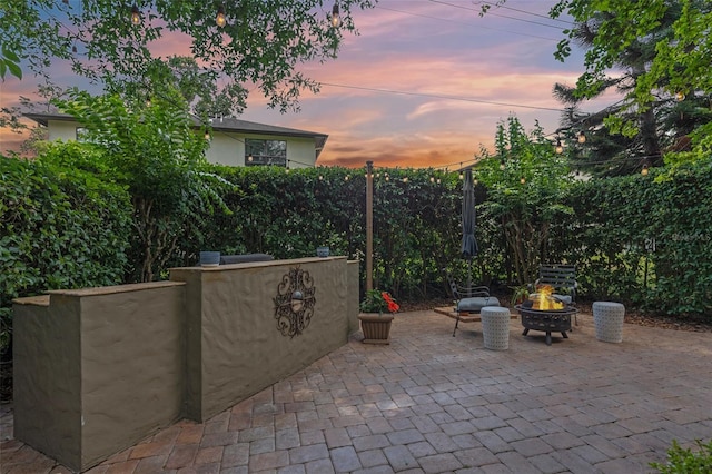 patio terrace at dusk featuring a fire pit and fence