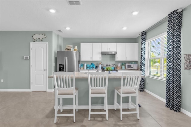 1555 Dawnview Way, Kissimmee, FL 34744 - kitchen with stainless steel appliances, under cabinet range hood, light countertops, an island with sink, and white cabinetry