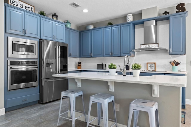 3865 W Stillwood Ln, Lake Mary, FL 32746 - kitchen with stainless steel appliances, blue cabinetry, wall chimney range hood, a breakfast bar area, and an island with sink