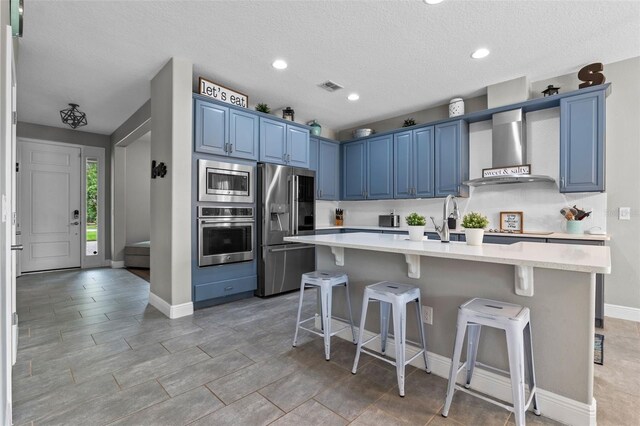3865 W Stillwood Ln, Lake Mary, FL 32746 - kitchen featuring stainless steel appliances, wall chimney range hood, blue cabinets, light countertops, and a textured ceiling