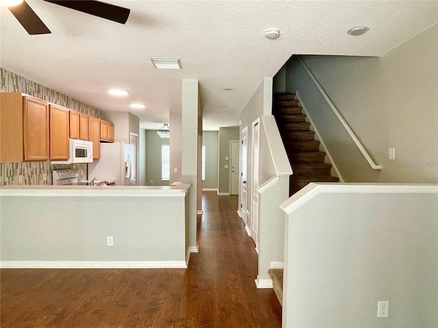 kitchen with white appliances, ceiling fan, dark wood-style flooring, a peninsula, and baseboards