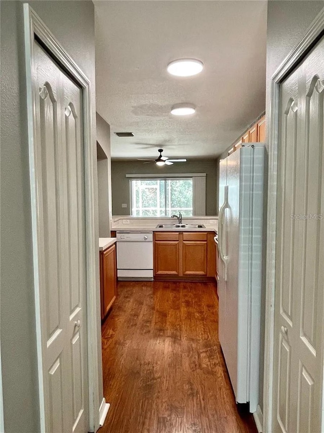kitchen featuring white appliances, a sink, dark wood finished floors, ceiling fan, and light countertops