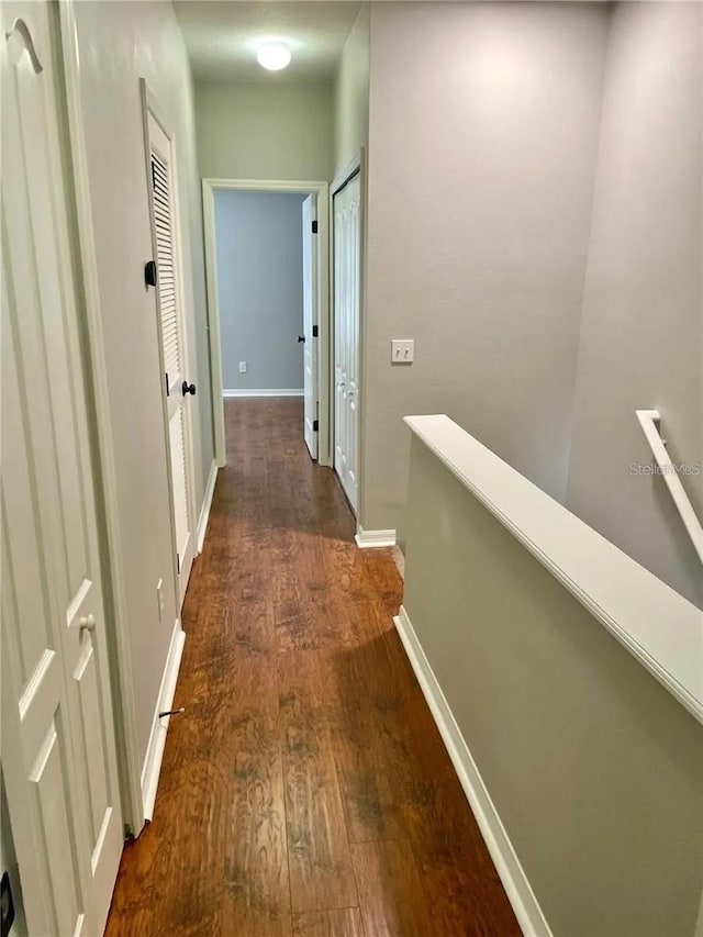 hall with an upstairs landing, dark wood-style flooring, and baseboards