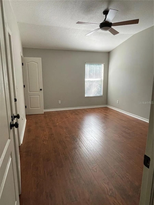 empty room with ceiling fan, dark wood-type flooring, baseboards, and a textured ceiling