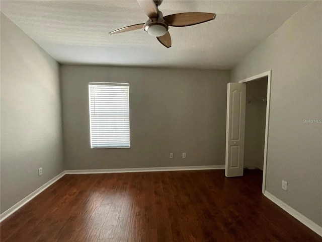 empty room featuring a ceiling fan, dark wood-type flooring, baseboards, and a textured ceiling