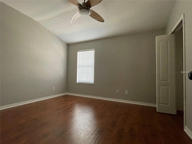 empty room with a ceiling fan, dark wood finished floors, baseboards, and vaulted ceiling