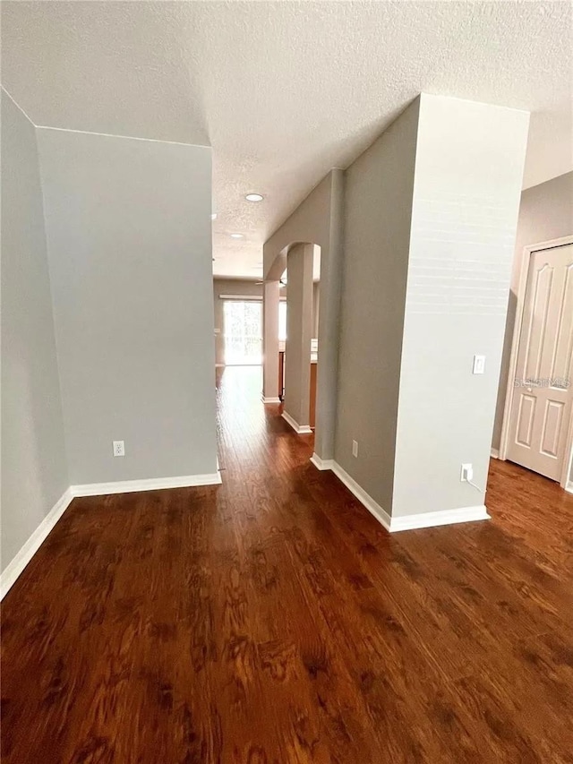 spare room featuring arched walkways, wood finished floors, a textured ceiling, and baseboards
