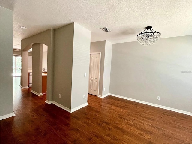 unfurnished room featuring arched walkways, wood finished floors, a textured ceiling, a chandelier, and baseboards