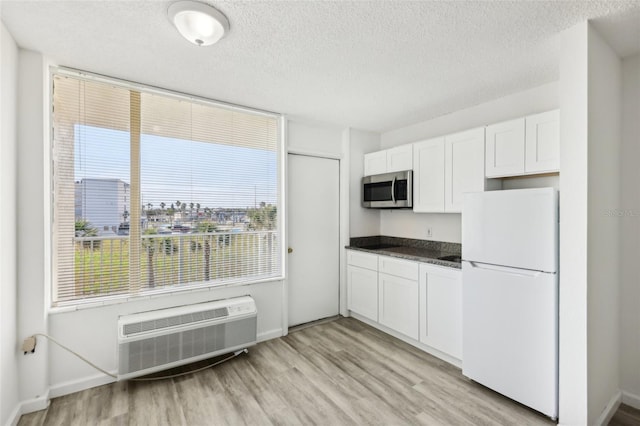 935 S Atlantic Ave Unit 302, Daytona Beach, FL 32118 - kitchen with freestanding refrigerator, stainless steel microwave, dark countertops, a wall unit AC, and light wood finished floors