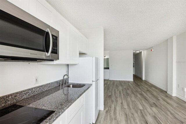 935 S Atlantic Ave Unit 302, Daytona Beach, FL 32118 - kitchen with stainless steel microwave, a sink, black electric stovetop, dark stone countertops, and light wood finished floors