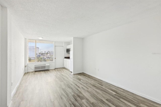 935 S Atlantic Ave Unit 302, Daytona Beach, FL 32118 - unfurnished living room with light wood finished floors, a textured ceiling, a wall mounted AC, and baseboards