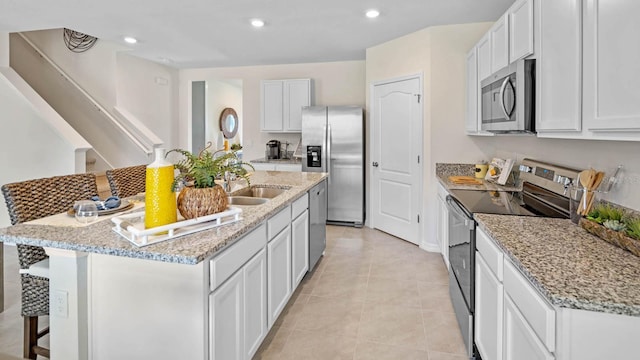 kitchen featuring appliances with stainless steel finishes, a sink, a center island with sink, white cabinetry, and light stone countertops