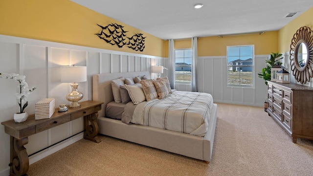 bedroom with light carpet, wainscoting, and a decorative wall