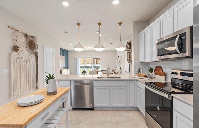 kitchen with stainless steel appliances, a sink, a peninsula, tasteful backsplash, and light tile patterned floors