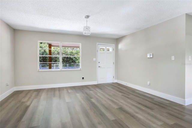 foyer entrance featuring wood finished floors, a textured ceiling, a chandelier, and baseboards