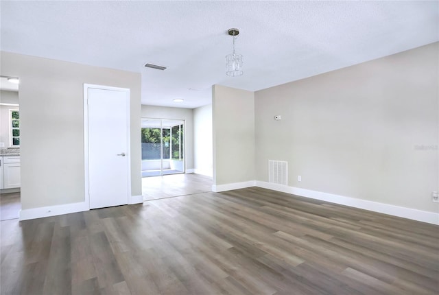 empty room featuring wood finished floors, baseboards, a chandelier, and a textured ceiling
