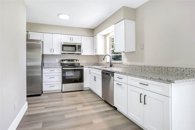 kitchen with appliances with stainless steel finishes, a sink, white cabinetry, and light stone countertops
