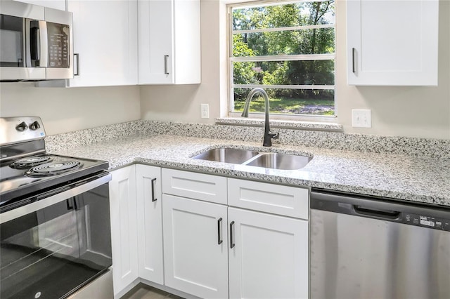 kitchen featuring stainless steel appliances, a sink, white cabinetry, and light stone counters