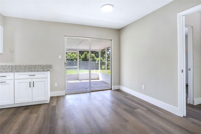 unfurnished dining area with dark wood-style flooring, baseboards, and a textured ceiling