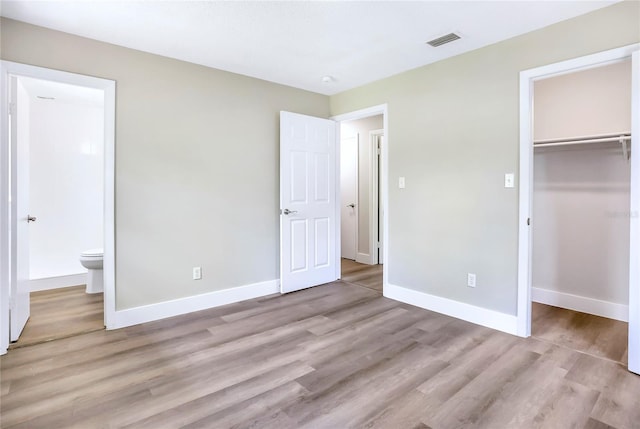 unfurnished bedroom featuring light wood finished floors, a spacious closet, and baseboards