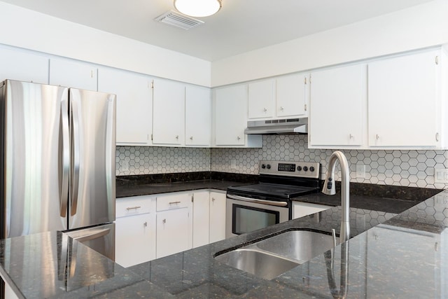 kitchen with appliances with stainless steel finishes, under cabinet range hood, dark stone countertops, and tasteful backsplash