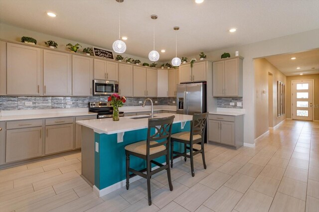 kitchen featuring appliances with stainless steel finishes, a sink, tasteful backsplash, an island with sink, and light countertops