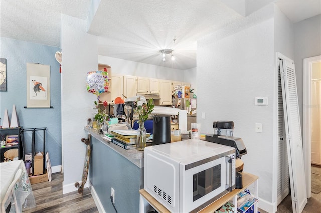kitchen featuring white microwave, a textured wall, baseboards, wood finished floors, and light countertops