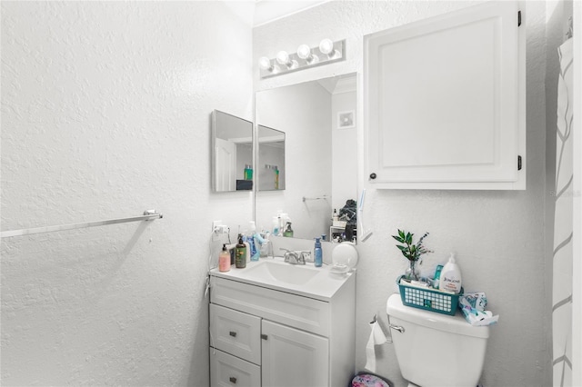 bathroom featuring a textured wall, vanity, and toilet